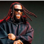 A crowd at a concert venue with bright stage lights, Burna Boy performing on stage at a packed outdoor event in Nairobi.