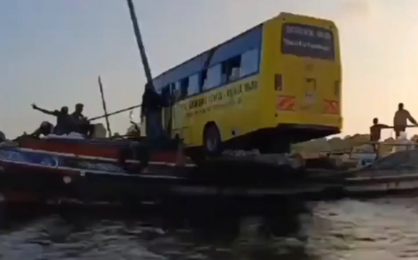 A school bus loaded onto a wooden boat floating on water in Lamu County, Kenya, surrounded by locals watching the transportation process.